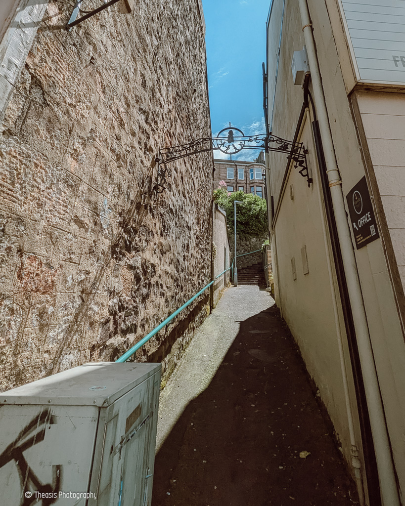 The bottom of the path up the cliff from Kempock Street with a metal sign arching over indicating the path to the stone.