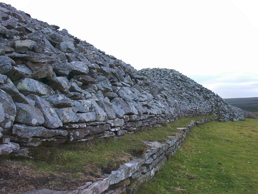 The west face of the long cairn from the north end.  Note the lower wall on which is built the upper wall on top of which is piled the cairn material.  Further to the south it can be seen that the original southerly round cairn extended beyond the later additions.