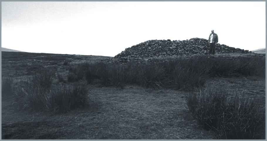 The cairn, looking southwest.  The yardstick is five feet nine inches tall and is standing on an area levelled by robbing about half way up the height of the cairn.