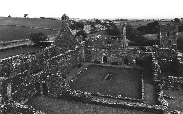Looking east over the abbey from the gatehouse.  The rectangular well can be seen in the centre of the cloister.  To the left of the cloister is the church.  In the wall at the far side of the cloister can be seen (from the left) the entrance to the chapter house, the entrance to the treasury, and a passageway leading through to the inner court.  To the right of the cloister can be seen the kitchen and dining room.  Beyond these, at the top right of the picture, is the towerhouse.