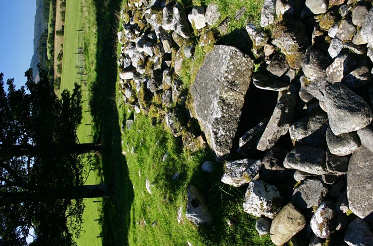 Looking west on the top of the cairn.  The burial space beneath the capstone can be seen, as can a flat edge of the slab forming the near wall of the cist.