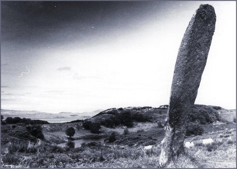 Looking north west over the Sound of Jura with the Isle of Jura in the background. The remains of a dun stands on the low hill to the right of the megalith.