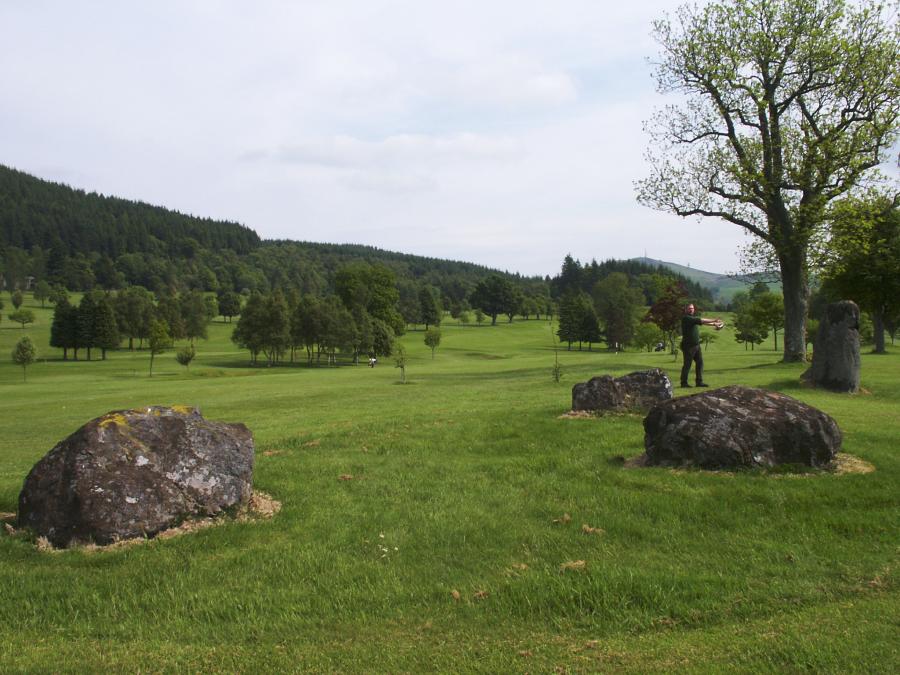 Looking northeast.  The three remaining stones of the circle are in the foreground, the standing stone near the tree is one of the outliers.  To the left of the outlier, the convenient yardstick stands about 2 metres tall.