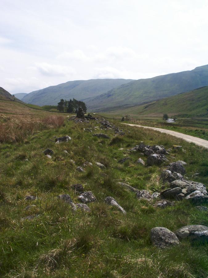 From the west end of the cairn looking southeast along Glen Almond.  A pyramidal pile of stones marks almost the east end of the cairn.  To the right of the point where the road first disappears, just past the far end of the cairn, a standing stone can be seen.