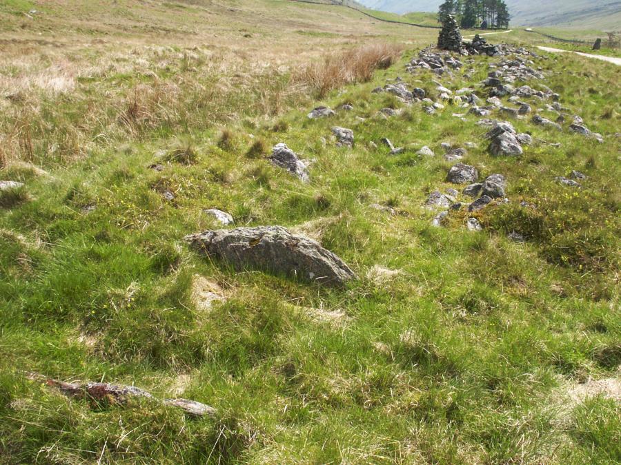 A cist in the centre of the cairn is in the foreground.  The standing stone is in the top-right of the picture.