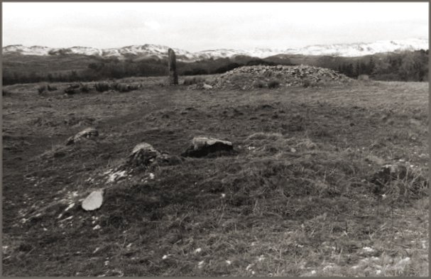 In the foreground is one cairn, another to the right of the monolith, and a third in the coarse grass to the left of the monolith.
